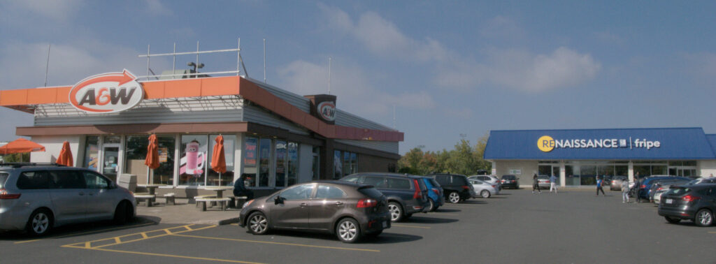 A wide shot of a commercial parking lot. To left is an A&W, to the right a thrift store. The wide format crop is meant to illustrate the 65:24 aspect ratio.